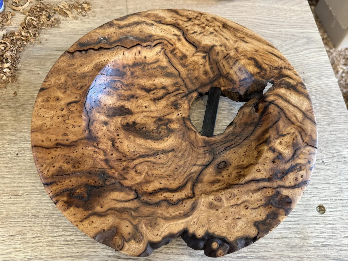 Turned burr wood bowl with a dark, swirling grain and a natural hole near the centre