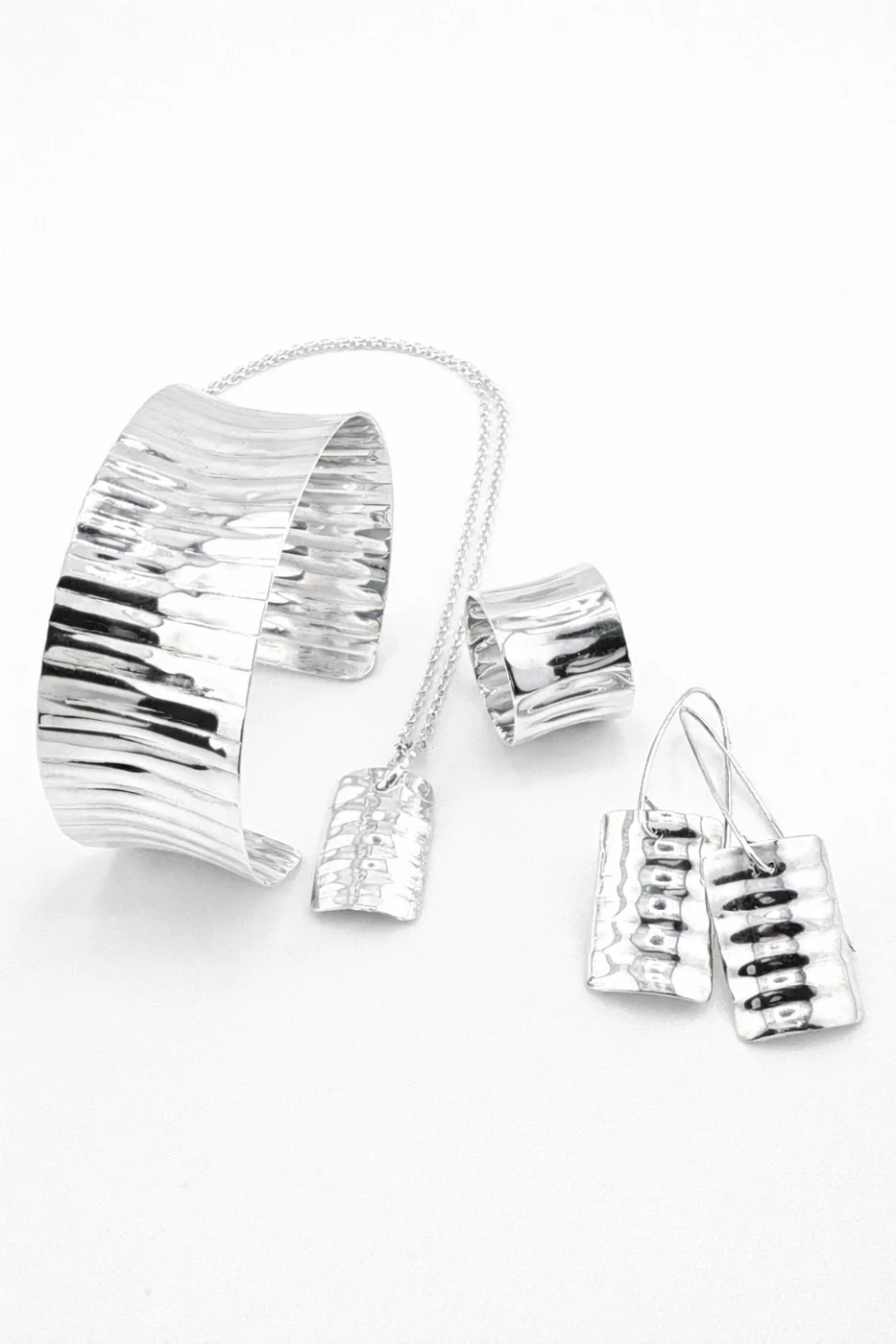 Polished silver cuff, ring, pendant and earrings with a rippled texture on a white background